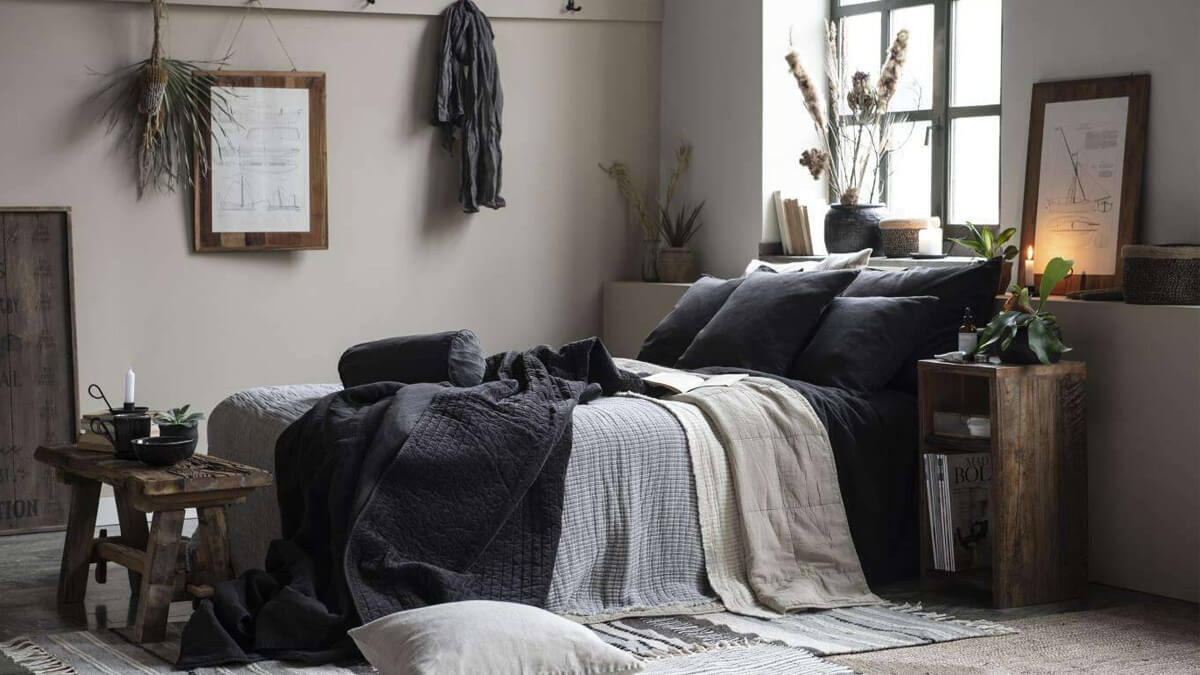 Hygge Schlafzimmer mit einem Bett mit dunklen Textilien und Deko an den Wänden und auf der Fensterbank