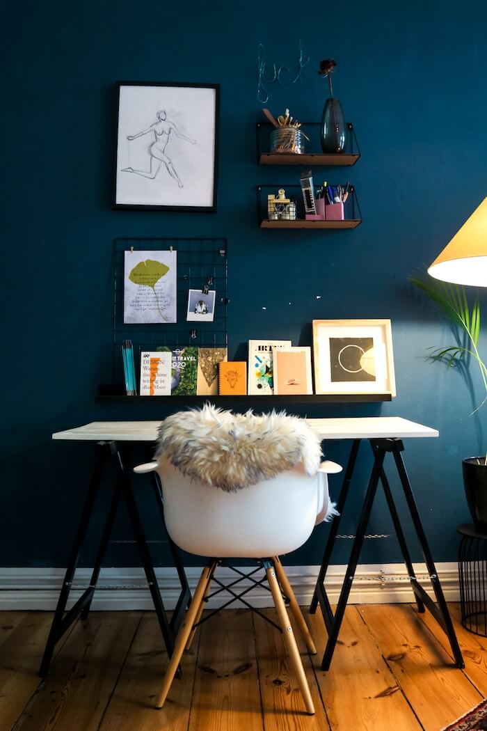 Home Office Möbel vor dunkelblauer Wand mit gemütlichem Schaffell auf derm weißen Stuhl