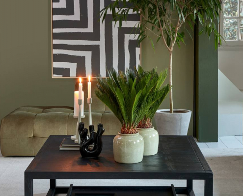 Riviera Maison Deko auf einem schwarzen Couchtisch mit Pflanzen, Bild Kerzenhaltern und Vase