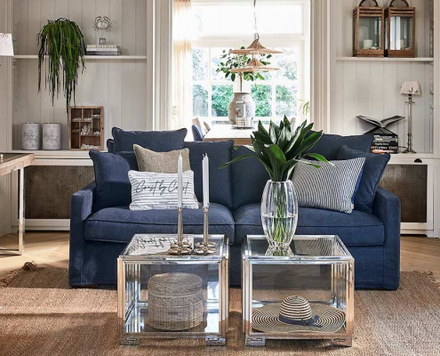 Blaues Riviera Maison Sofa im maritimen Einrichtungsstil in einem Wohnzimmer mit zwei silbernen Couchtischen und Deko