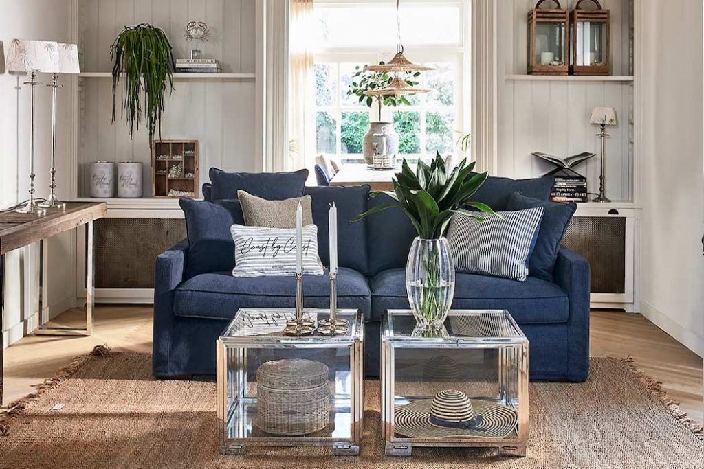 Blaues Riviera Maison Sofa im maritimen Einrichtungsstil in einem Wohnzimmer mit zwei silbernen Couchtischen und Deko